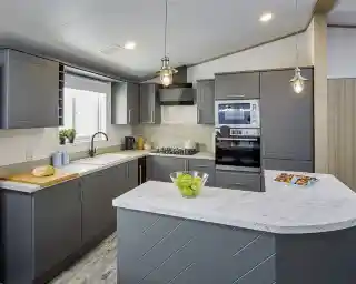 Modern kitchen in the Atlas Lilac Lodge with grey cabinetry, marble-style countertops, built-in oven, and peninsula breakfast bar.