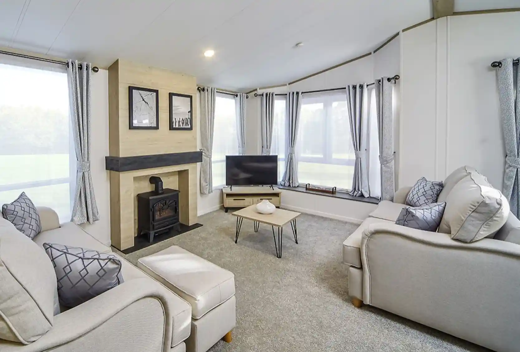 Bright lounge in the Atlas Lilac Lodge featuring large windows, neutral sofas, electric fireplace, and contemporary décor.