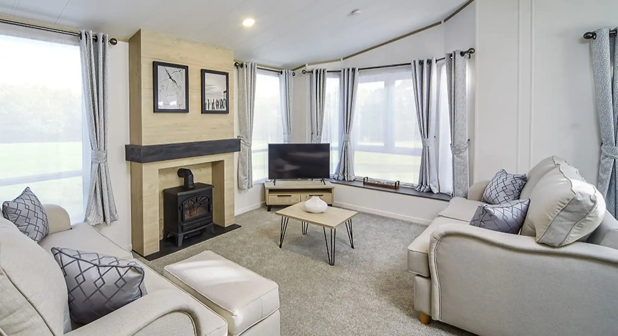 Bright lounge in the Atlas Lilac Lodge featuring large windows, neutral sofas, electric fireplace, and contemporary décor.