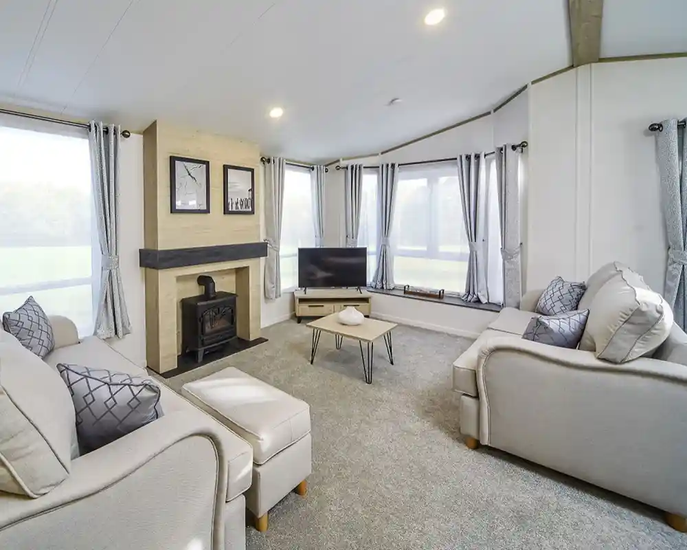 Bright lounge in the Atlas Lilac Lodge featuring large windows, neutral sofas, electric fireplace, and contemporary décor.