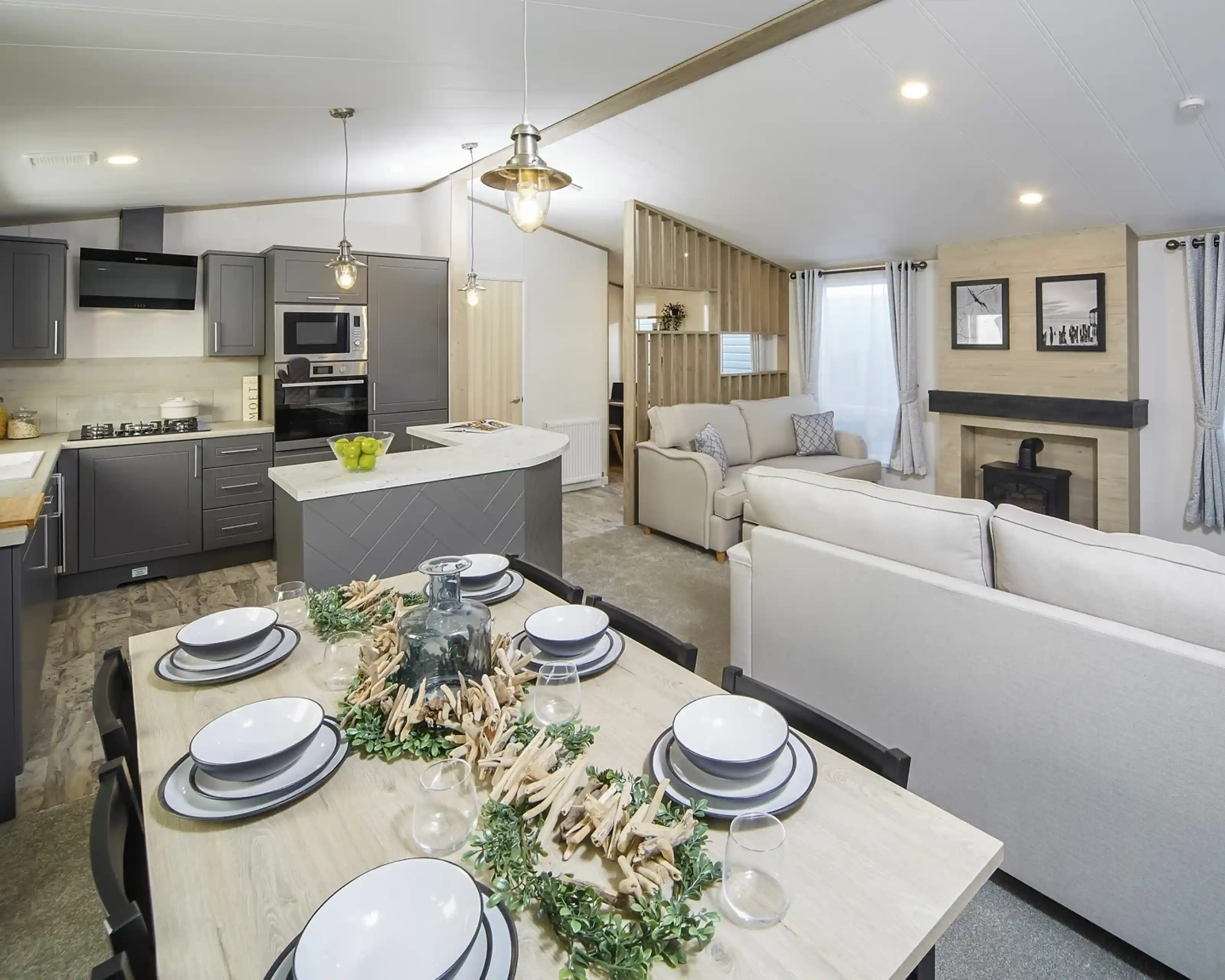 Modern open-plan kitchen, dining, lounge area in the Atlas Lilac Lodge with grey cabinetry, light wood dining table and chairs and neutral sofas.