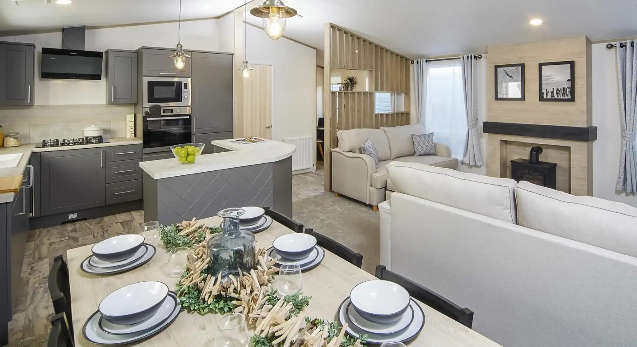 Modern open-plan kitchen, dining, lounge area in the Atlas Lilac Lodge with grey cabinetry, light wood dining table and chairs and neutral sofas.