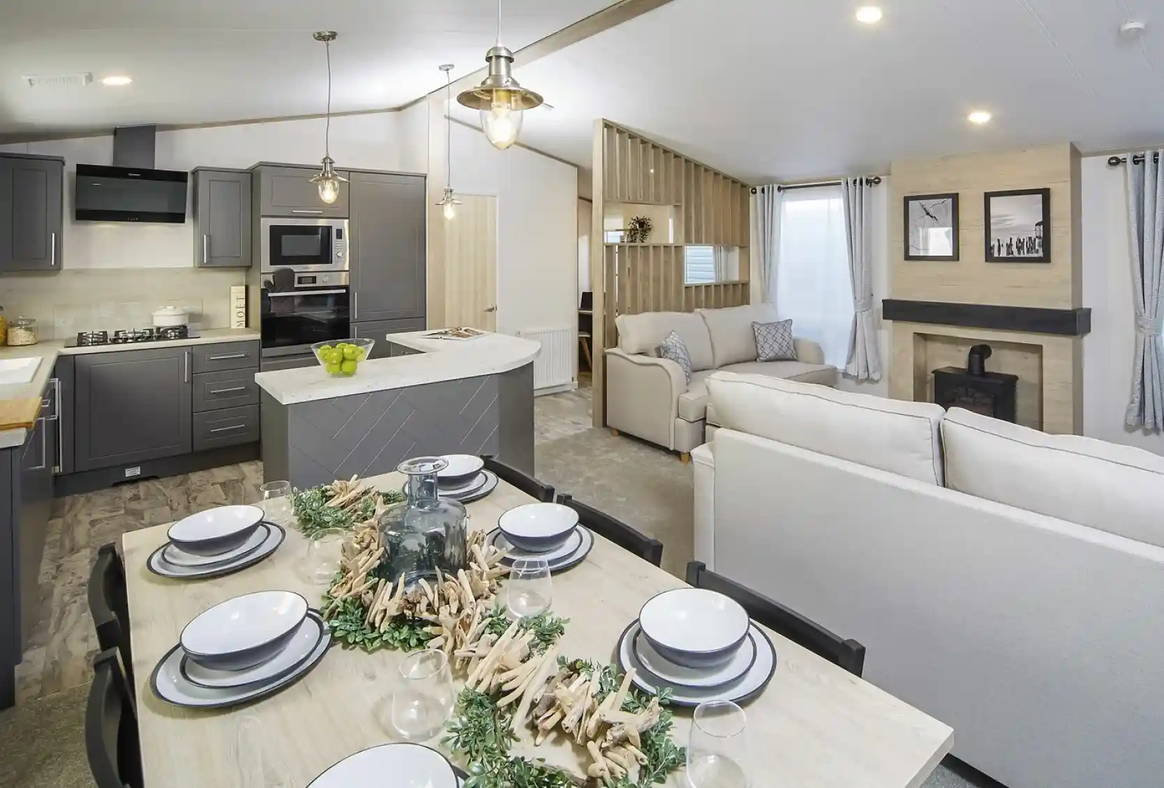 Modern open-plan kitchen, dining, lounge area in the Atlas Lilac Lodge with grey cabinetry, light wood dining table and chairs and neutral sofas.