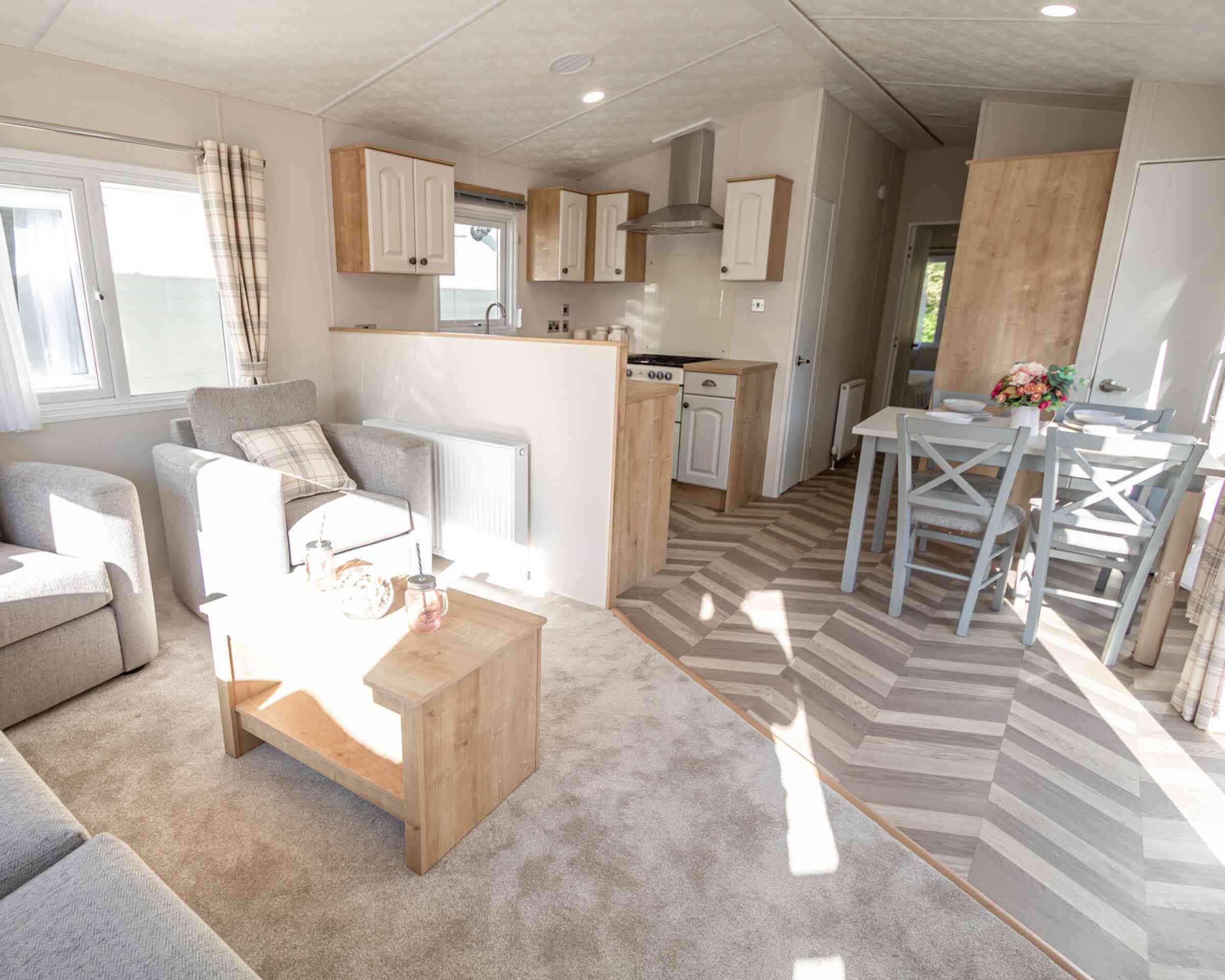 Interior view of a caravan showcasing a living room and kitchen dining area with contemporary decor and ample natural light.