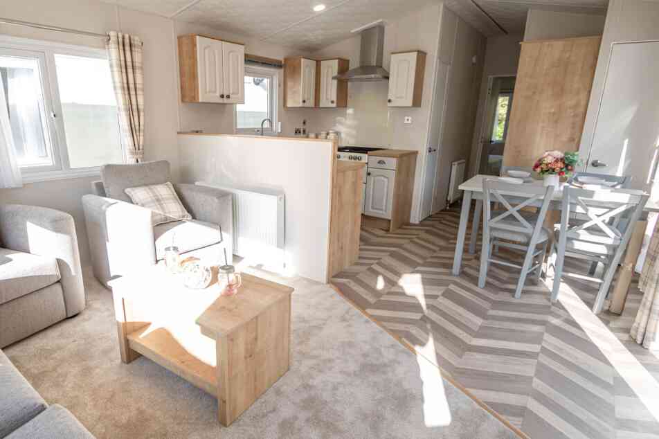 Interior view of a caravan showcasing a living room and kitchen dining area with contemporary decor and ample natural light.