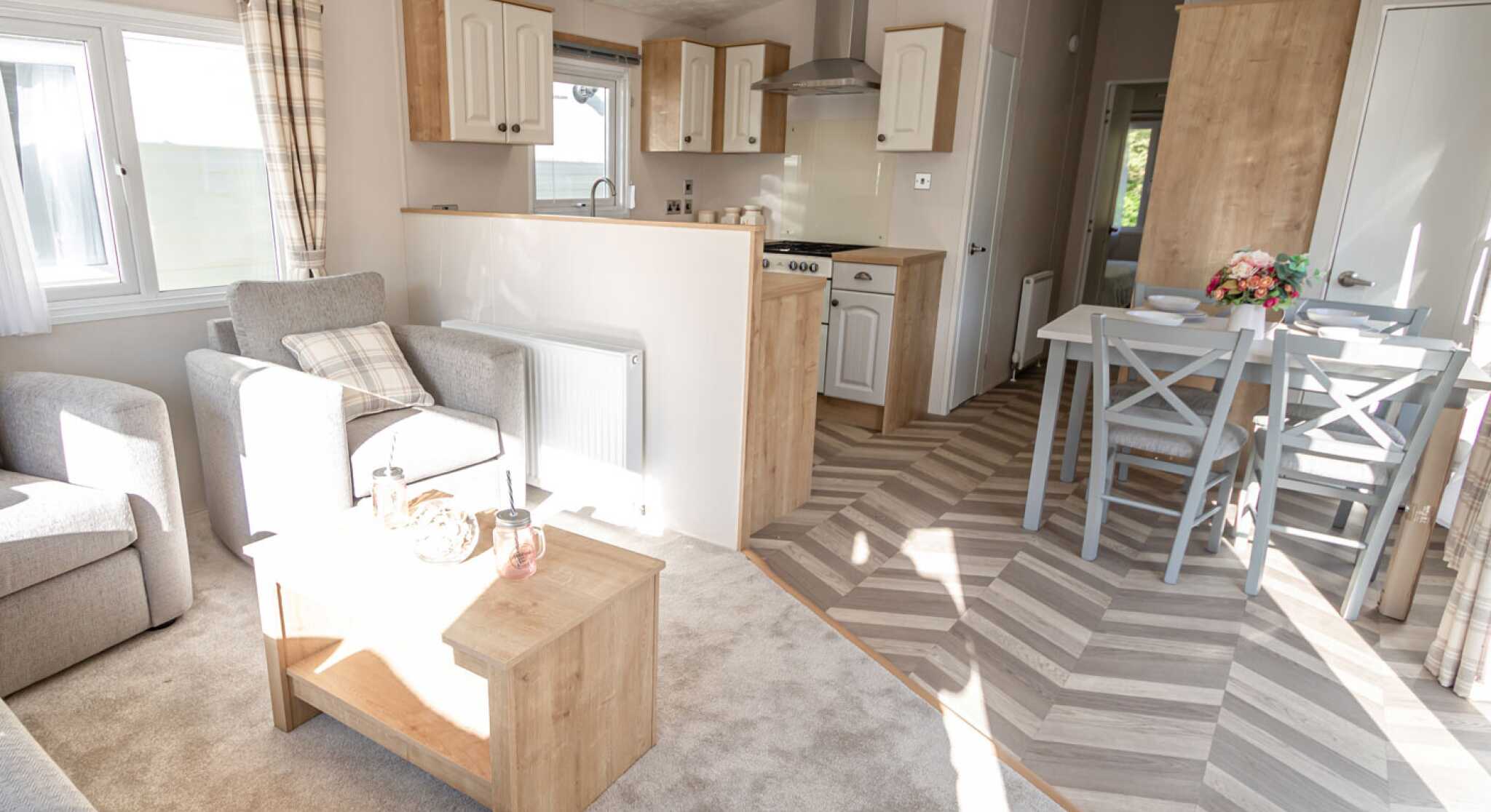 Interior view of a caravan showcasing a living room and kitchen dining area with contemporary decor and ample natural light.