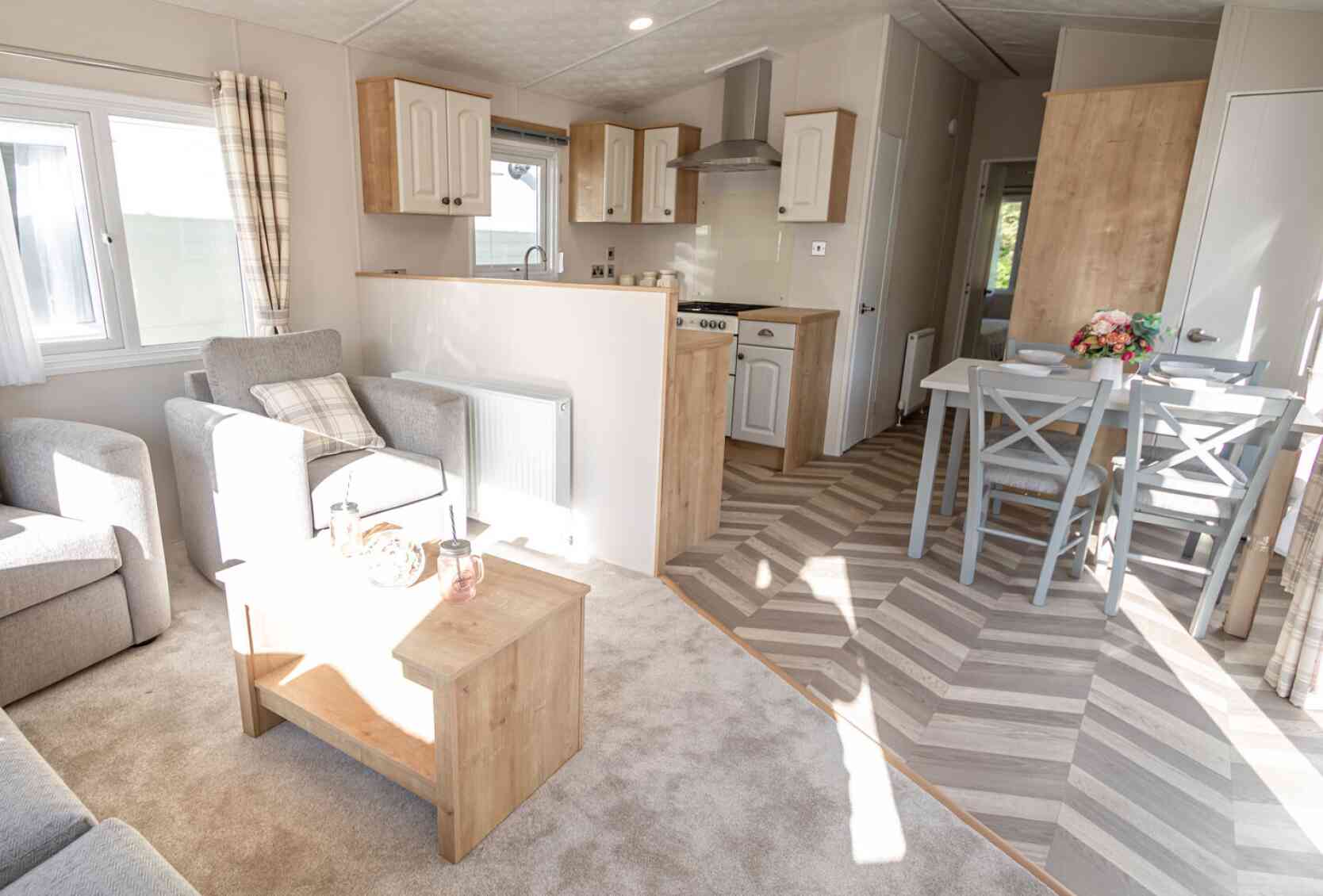 Interior view of a caravan showcasing a living room and kitchen dining area with contemporary decor and ample natural light.