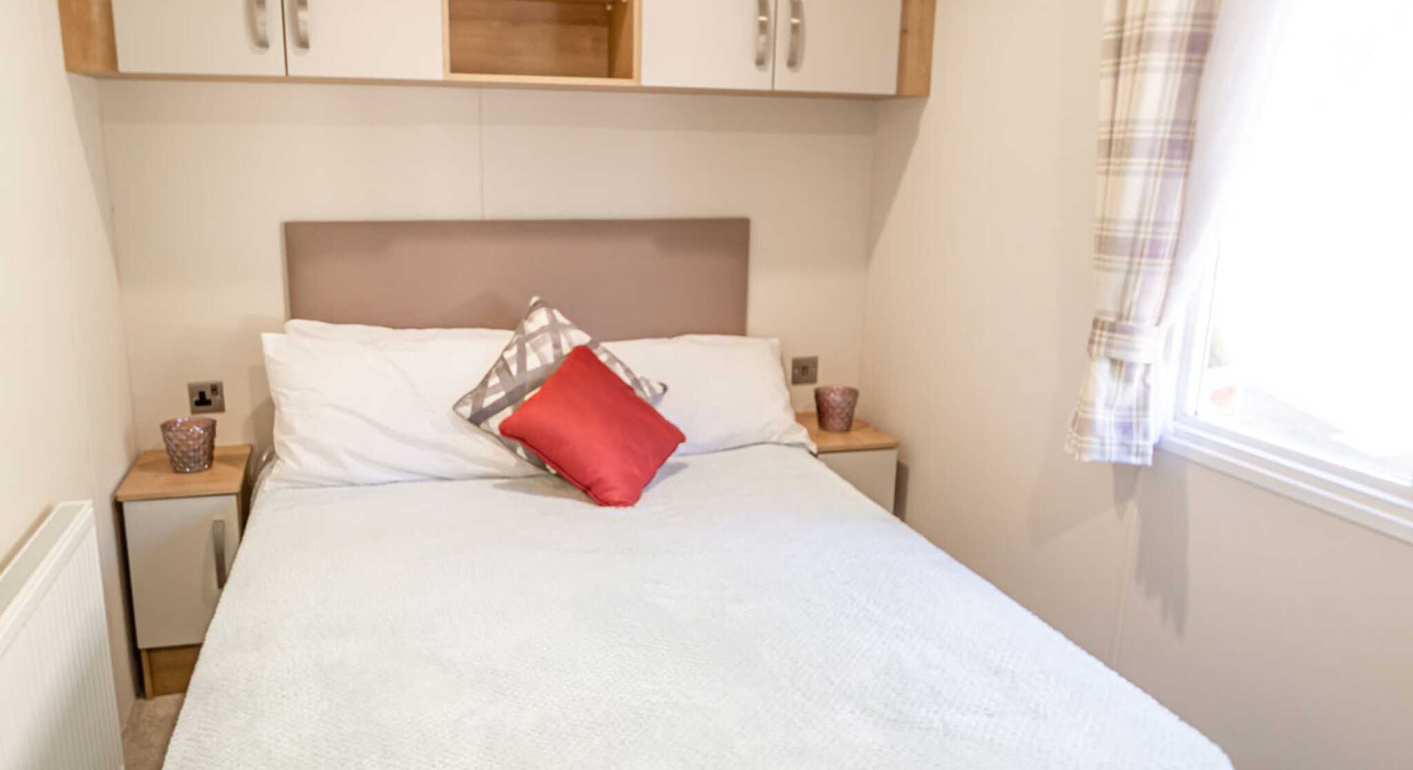 A cosy bedroom featuring a double bed, two bedside tables and overhead storage, creating a functional sleeping space.