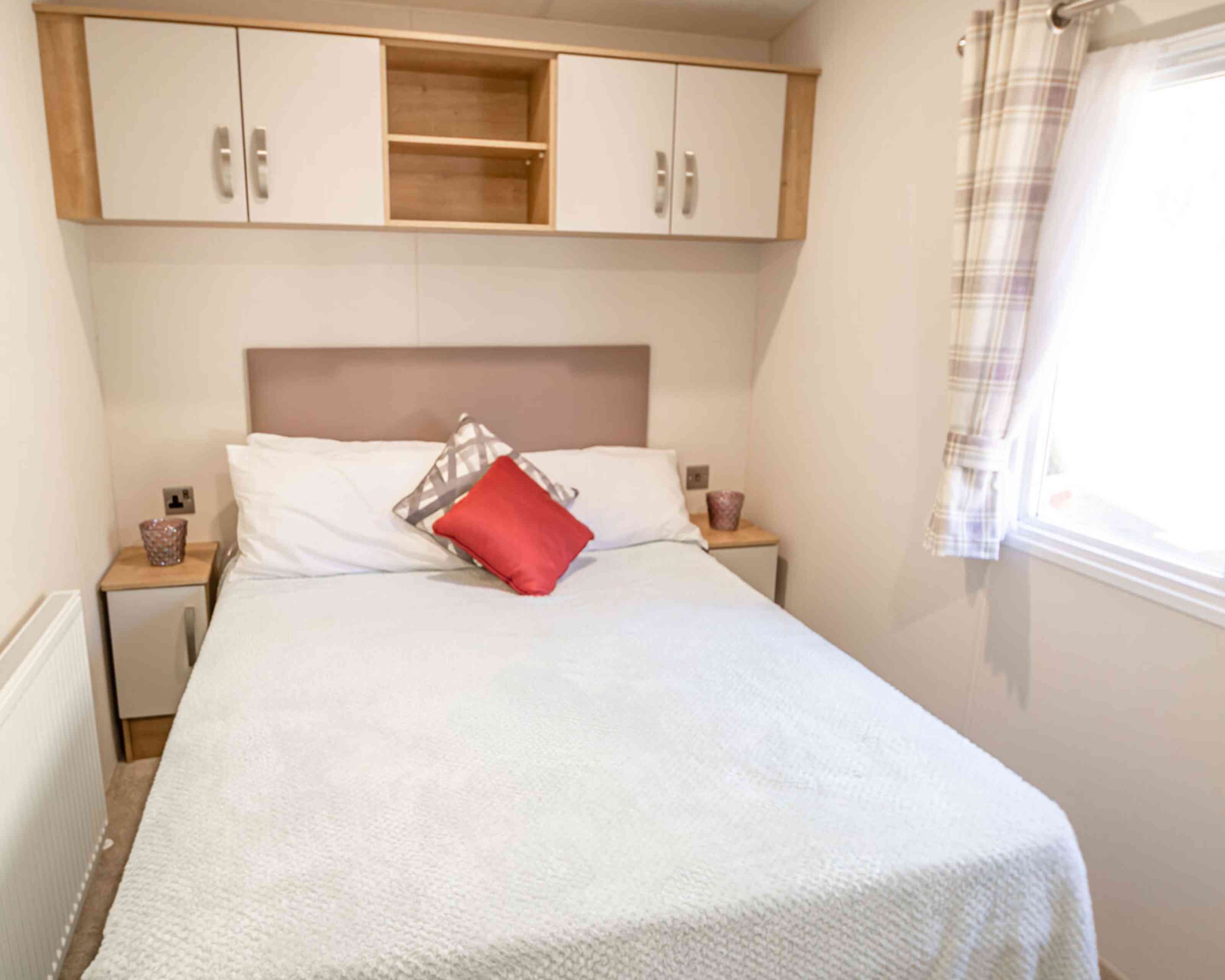A cosy bedroom featuring a double bed, two bedside tables and overhead storage, creating a functional sleeping space.