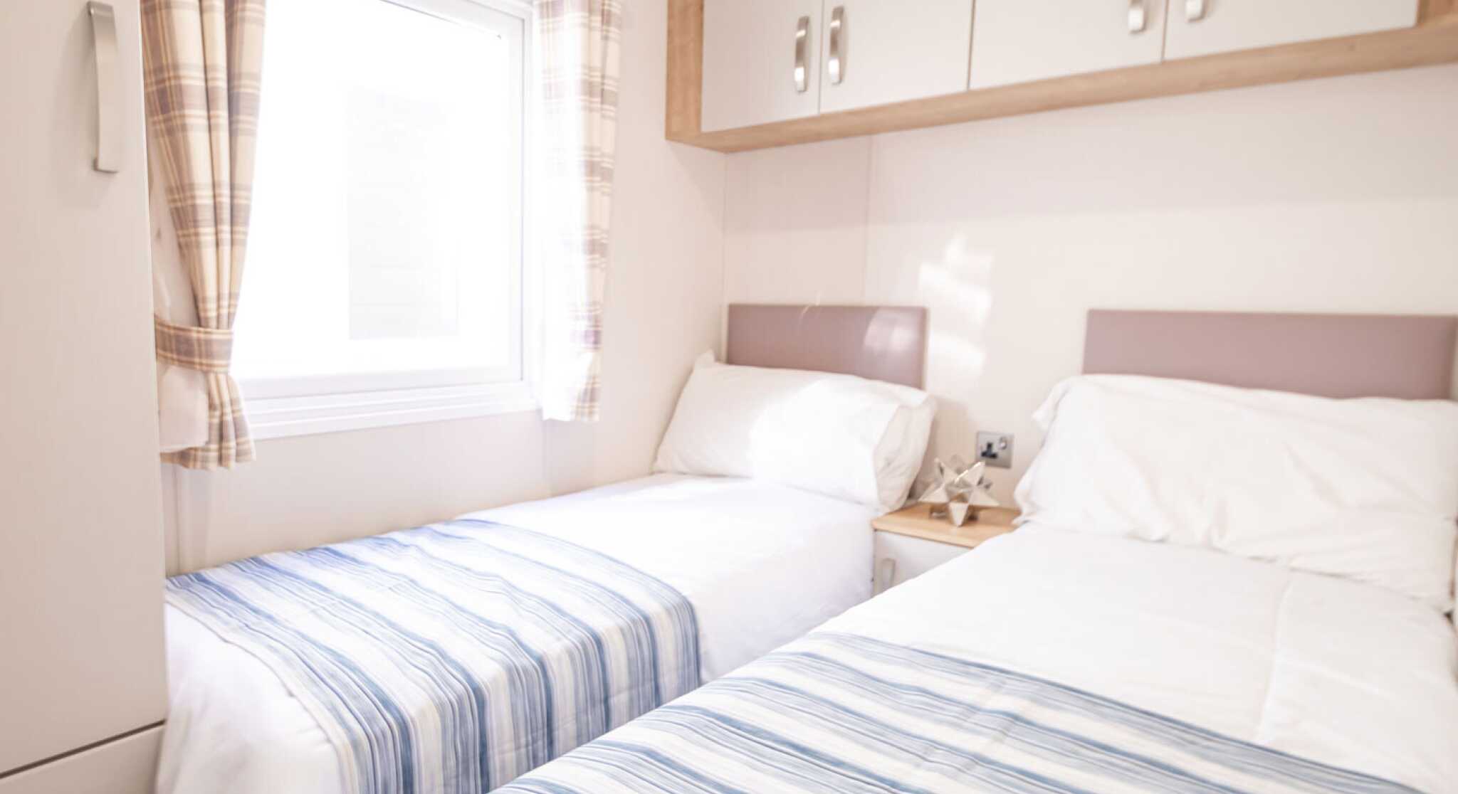 A bedroom with twin beds, overhead storage and wardrobe, together with a window.