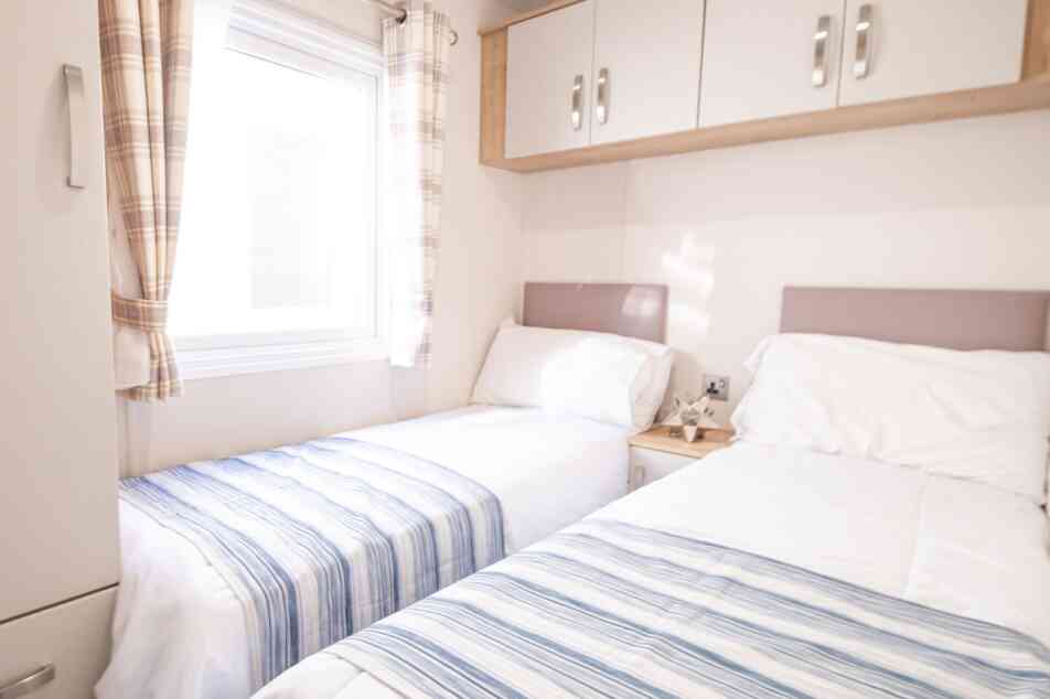 A bedroom with twin beds, overhead storage and wardrobe, together with a window.