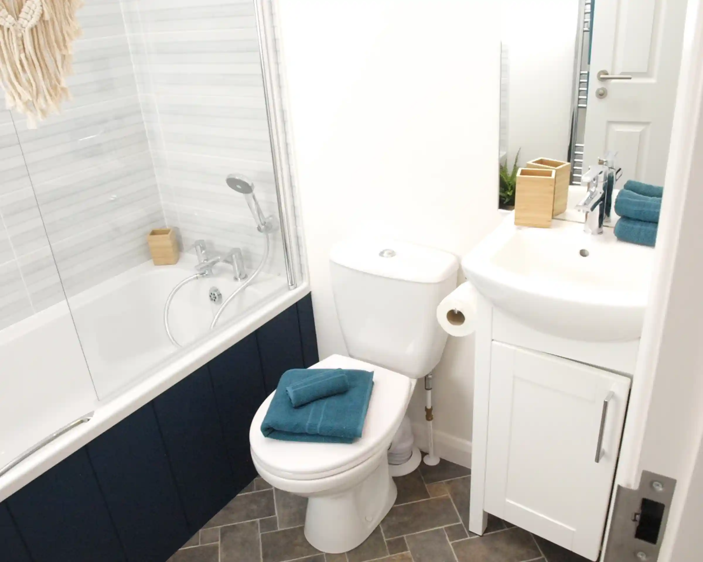 Bath with shower over and shower screen, together with WC and wash basin with vanity unit in a bright bathroom