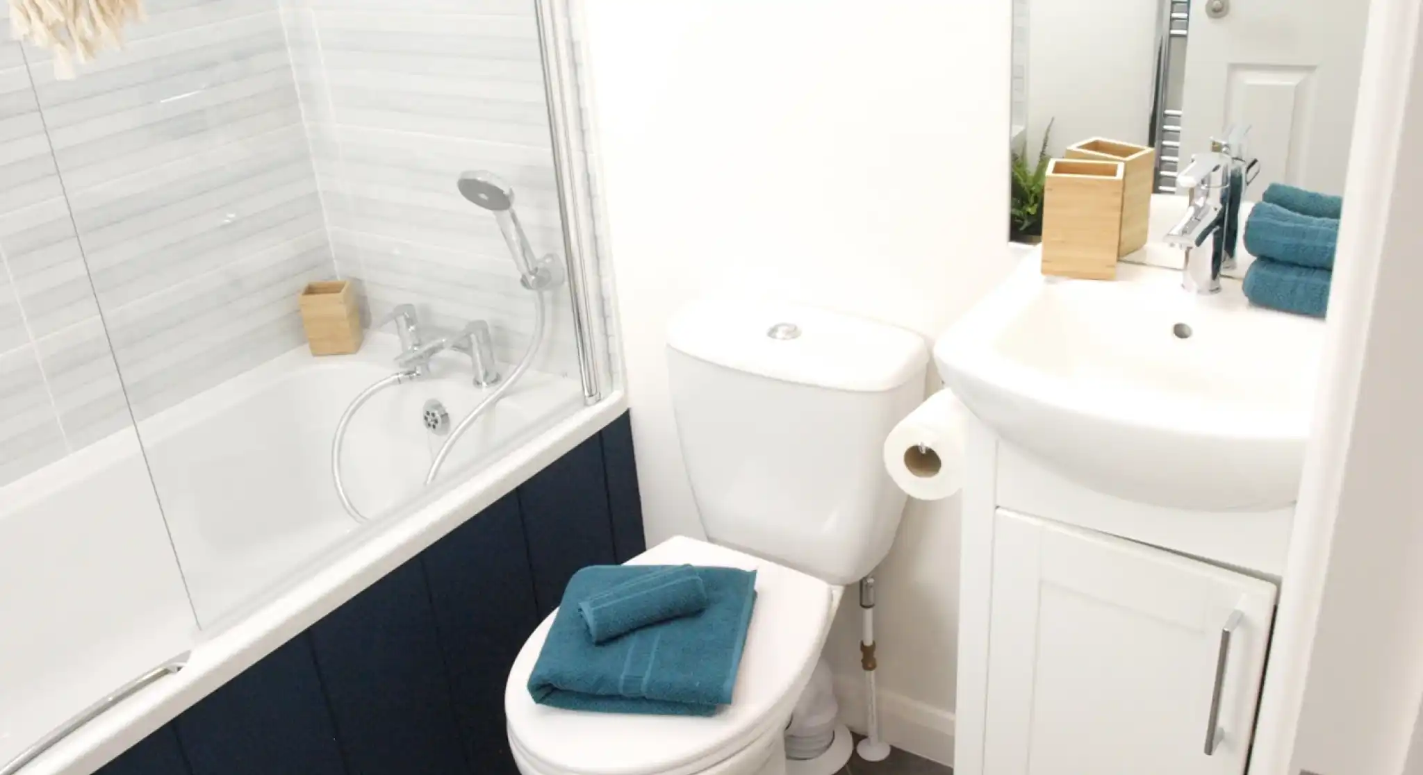 Bath with shower over and shower screen, together with WC and wash basin with vanity unit in a bright bathroom