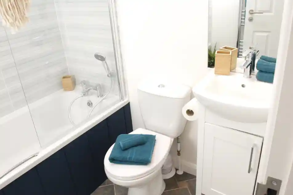 Bath with shower over and shower screen, together with WC and wash basin with vanity unit in a bright bathroom