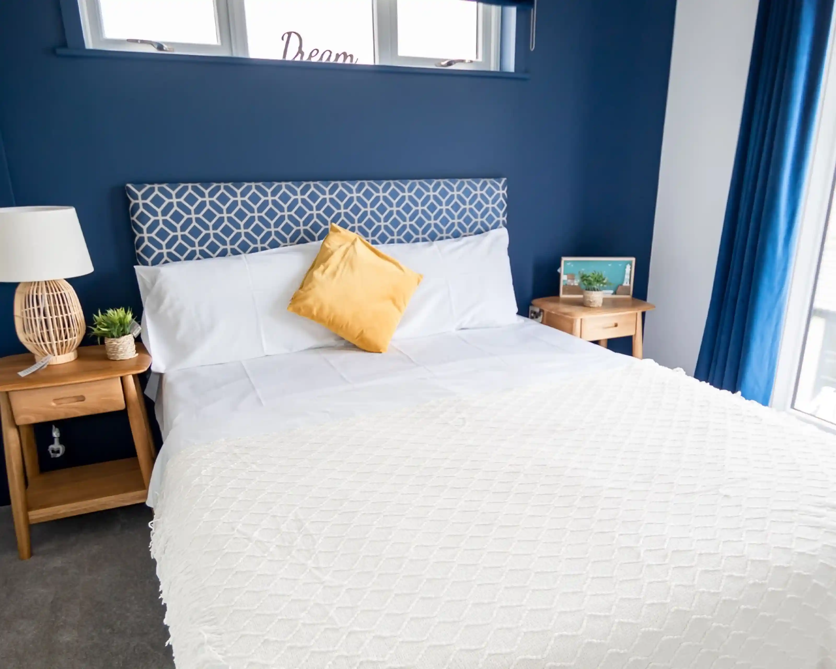 Double bedroom with white sheets and blue feature wall behind headboard, together with two night stands