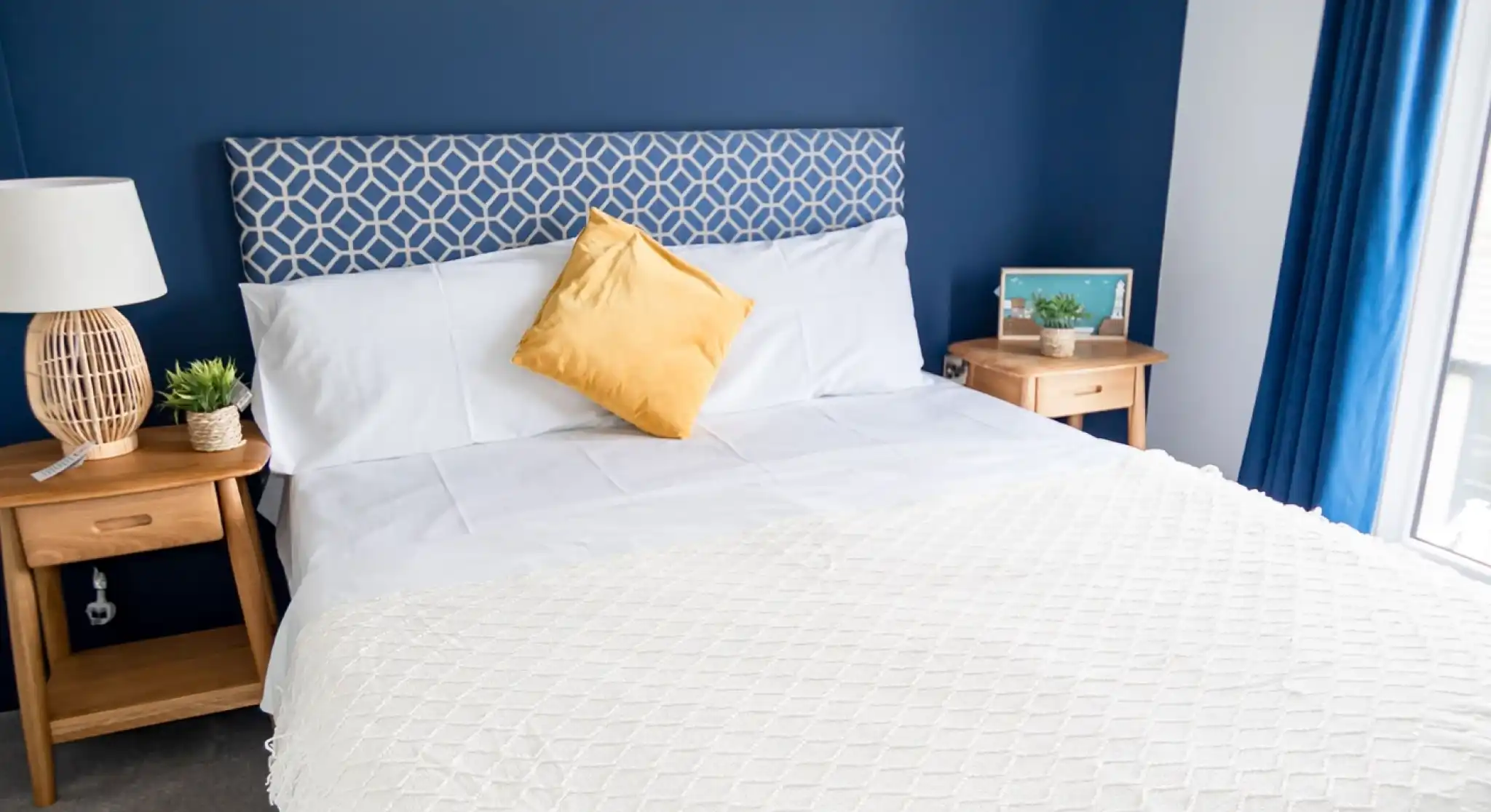 Double bedroom with white sheets and blue feature wall behind headboard, together with two night stands