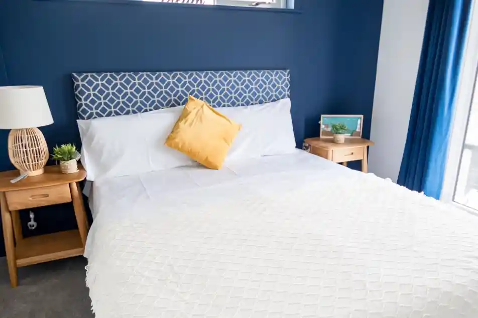 Double bedroom with white sheets and blue feature wall behind headboard, together with two night stands