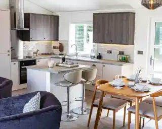 Open plan kitchen, dining, living room with light grey oak style and cream cabinetry and Scandinavian style dining table