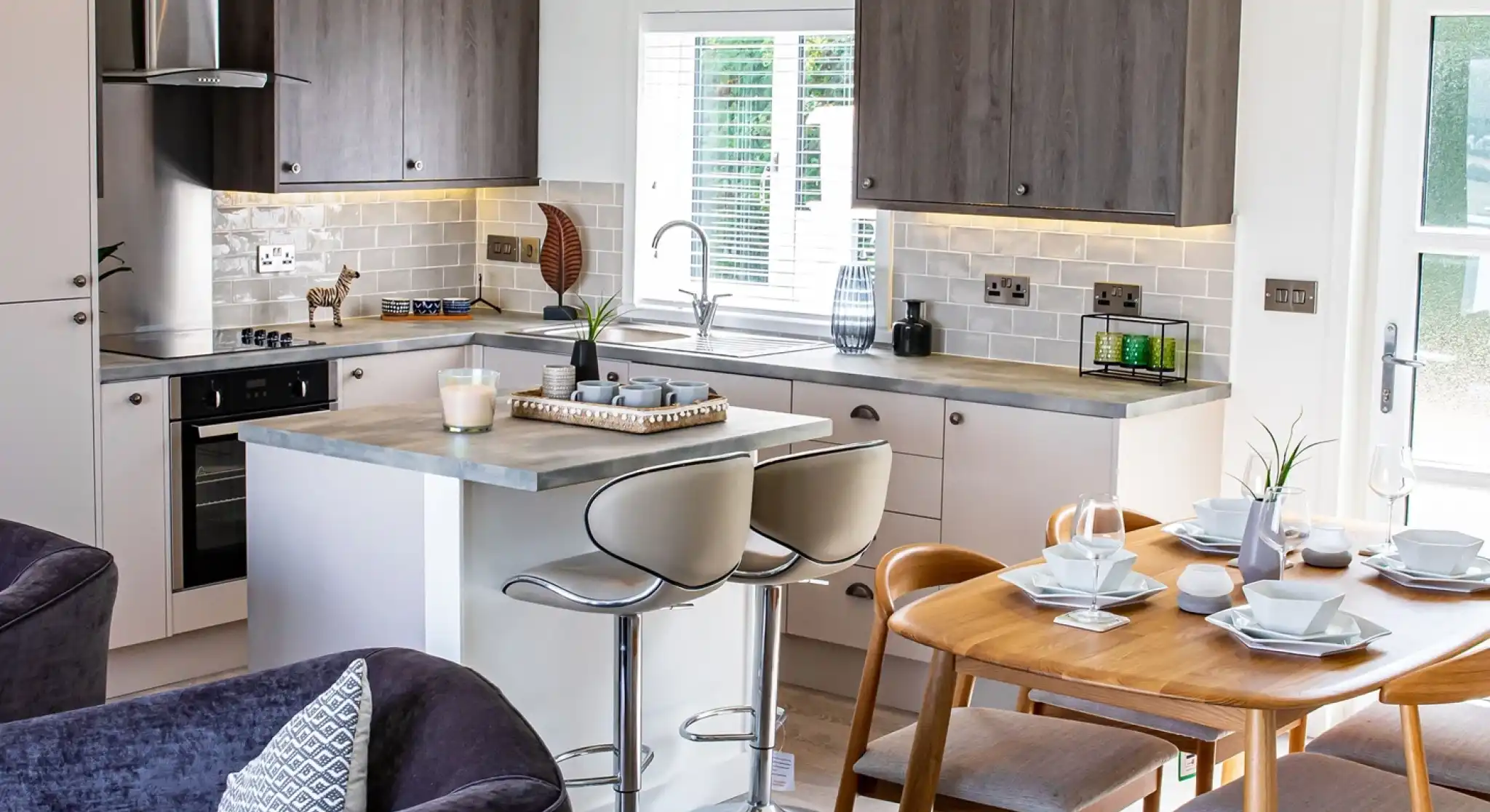 Open plan kitchen, dining, living room with light grey oak style and cream cabinetry and Scandinavian style dining table