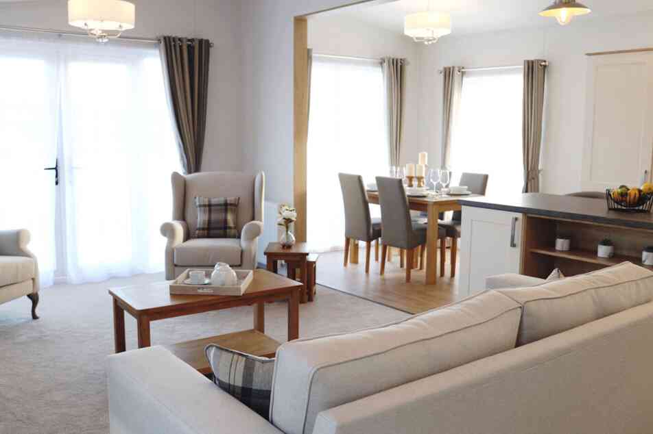 A cosy living room featuring a sofa, table, chair, and an adjoining kitchen area.