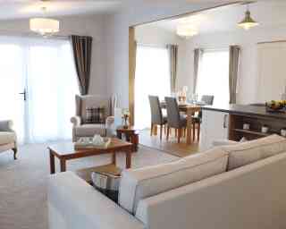 A cosy living room featuring a sofa, table, chair, and an adjoining kitchen area.