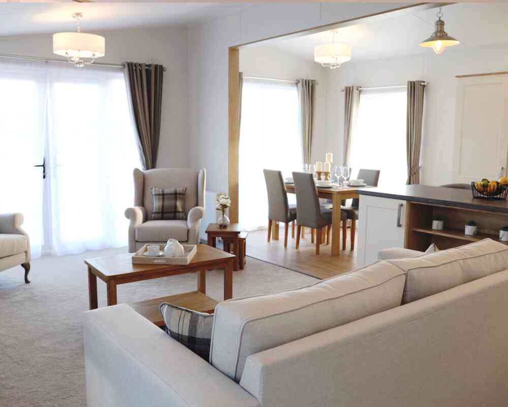 A cosy living room featuring a sofa, table, chair, and an adjoining kitchen area.