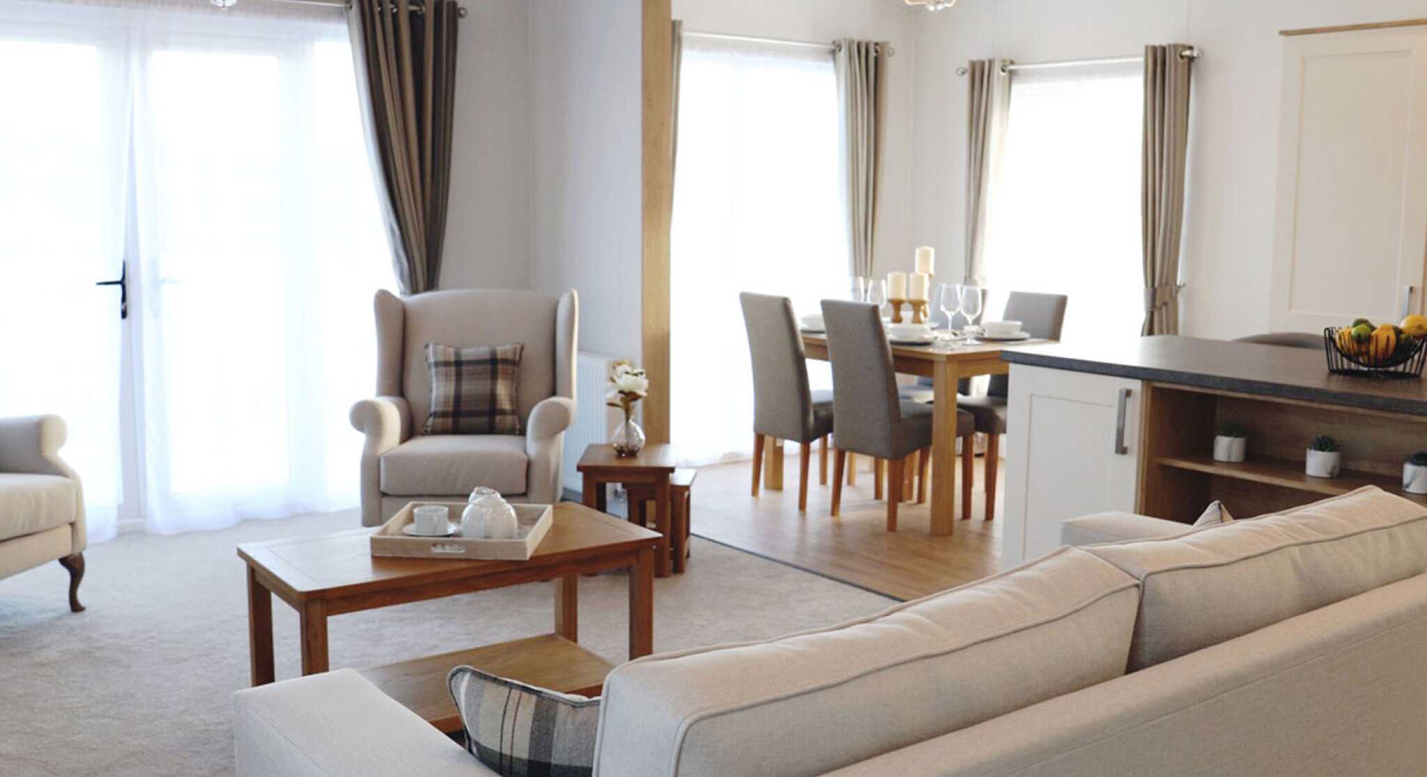 A cosy living room featuring a sofa, table, chair, and an adjoining kitchen area.