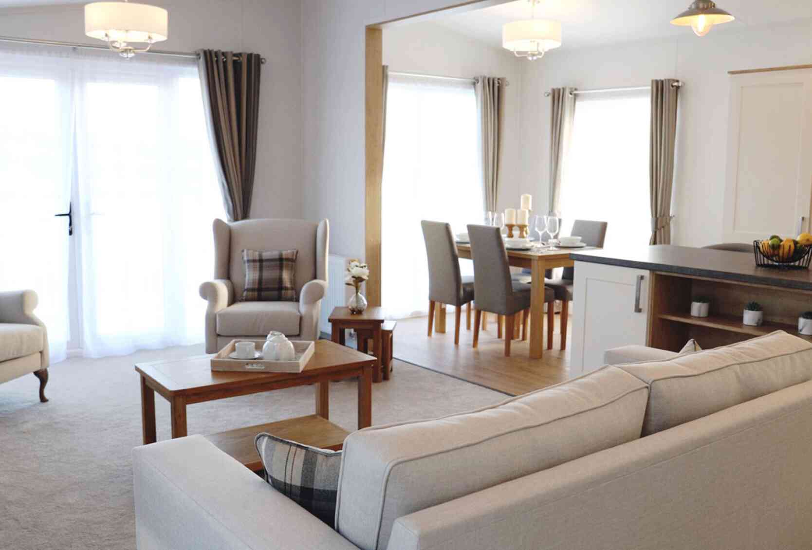 A cosy living room featuring a sofa, table, chair, and an adjoining kitchen area.