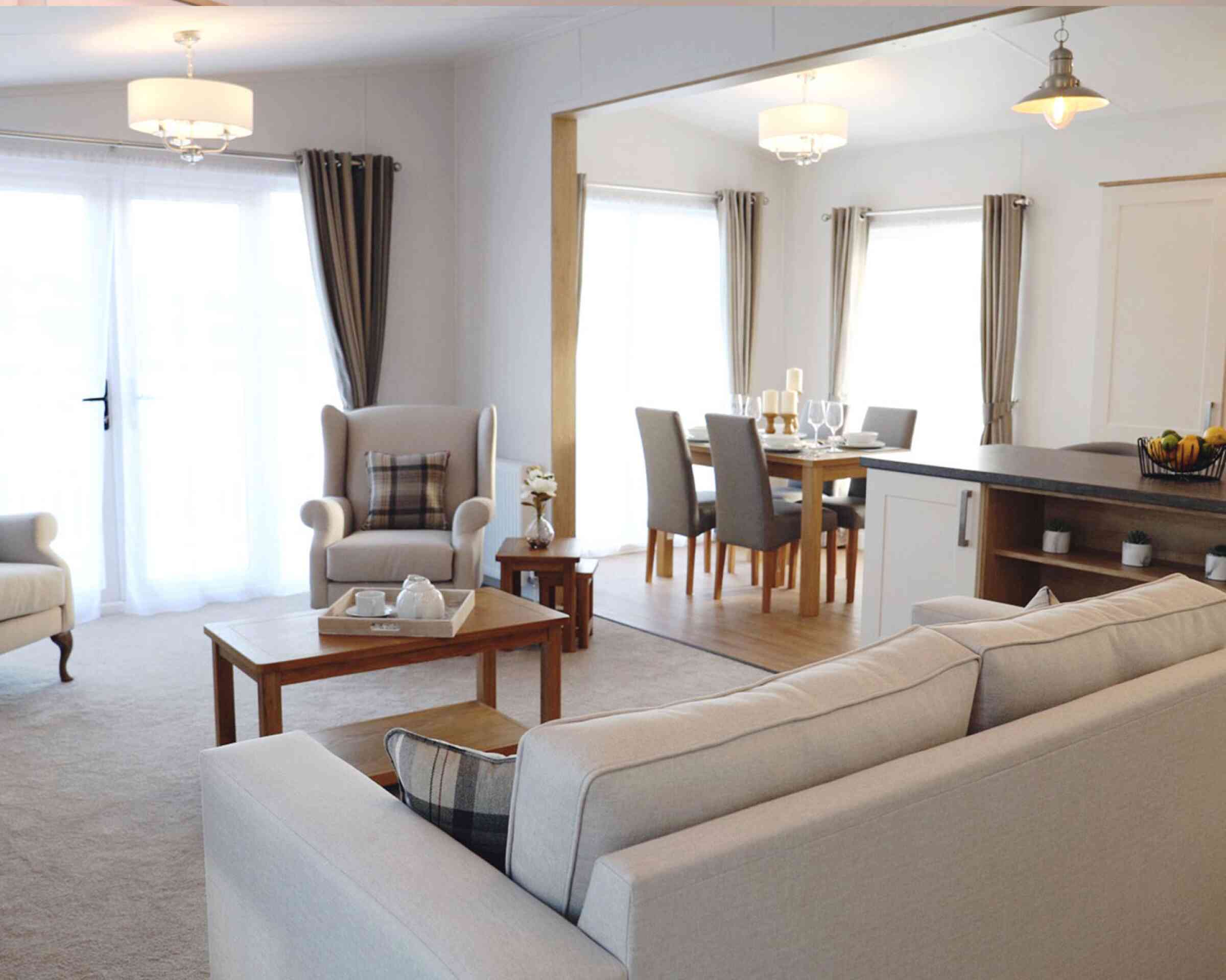 A cosy living room featuring a sofa, table, chair, and an adjoining kitchen area.