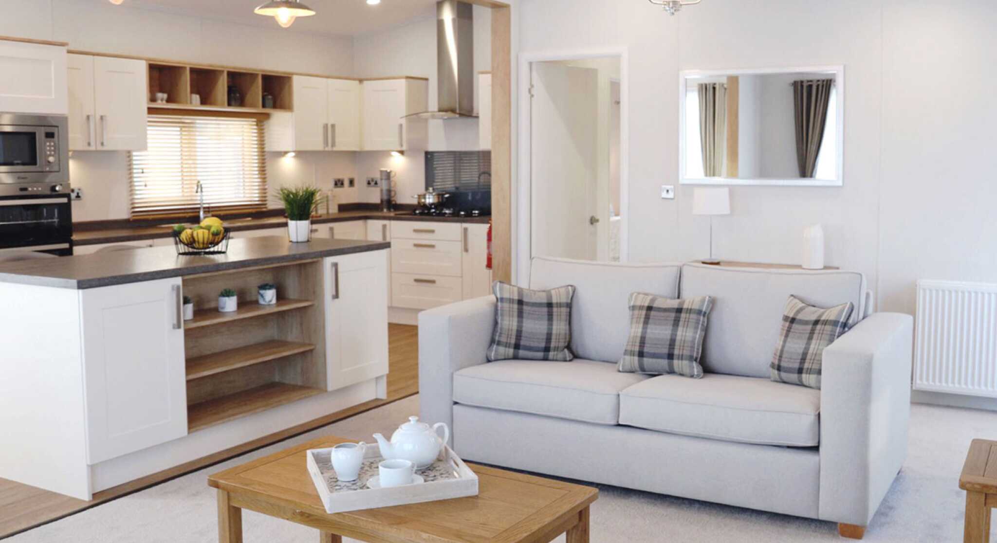 A living room scene with a comfortable sofa, a coffee table, and a glimpse of the kitchen area.