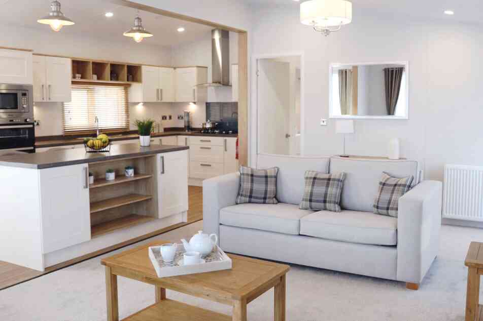 A living room scene with a comfortable sofa, a coffee table, and a glimpse of the kitchen area.