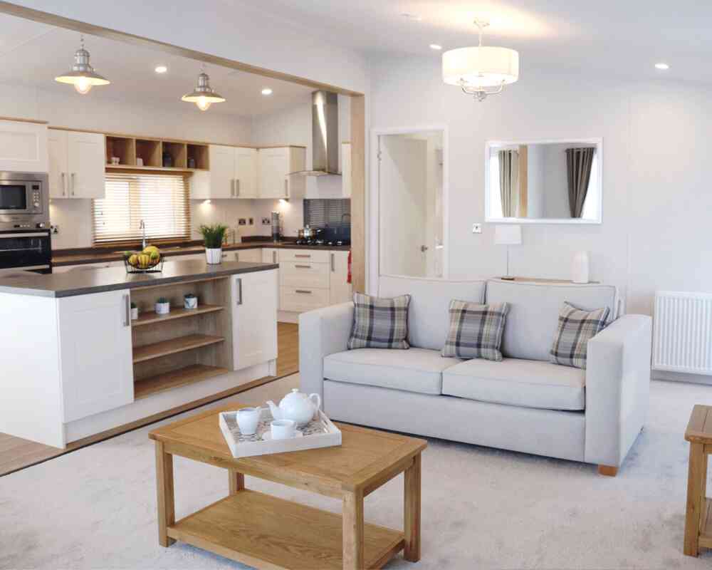 A living room scene with a comfortable sofa, a coffee table, and a glimpse of the kitchen area.