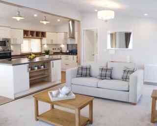 A living room scene with a comfortable sofa, a coffee table, and a glimpse of the kitchen area.