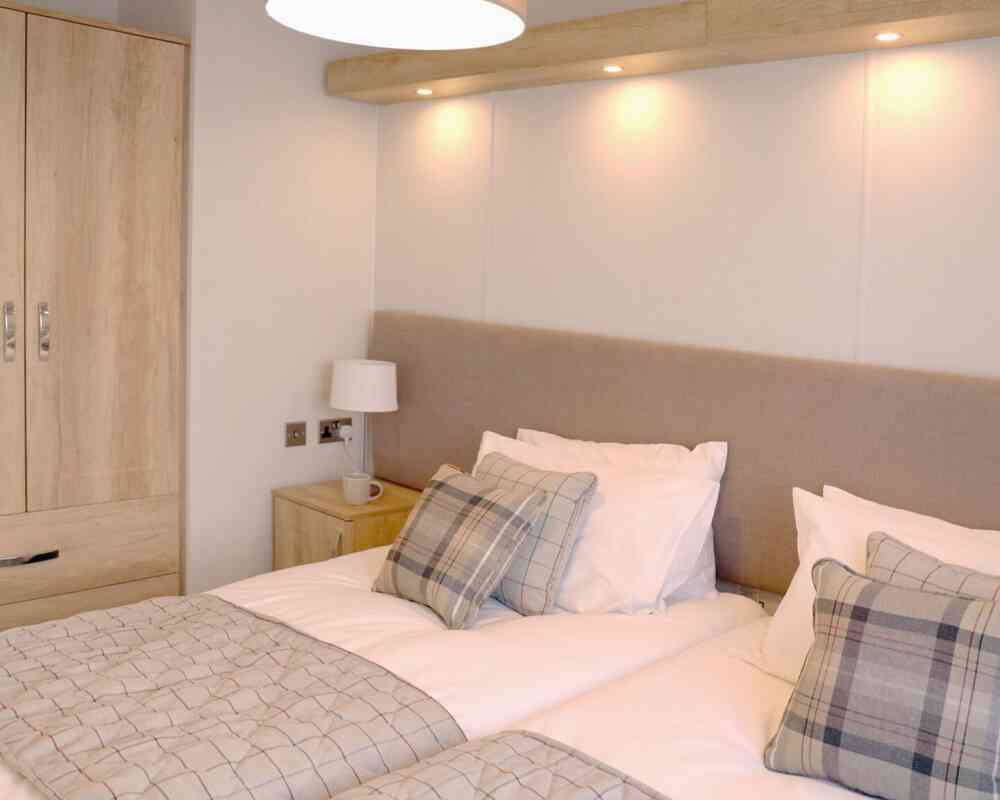 A well-furnished bedroom showcasing two beds and a wardrobe, designed for comfort and practicality.