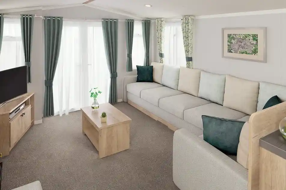 A modern living room featuring a spacious grey sectional sofa with light green and teal throw pillows. There is a wooden coffee table in the center and a television on a wooden stand. Natural light streams in through sheer curtains, illuminating the space adorned with leafy patterned drapes.