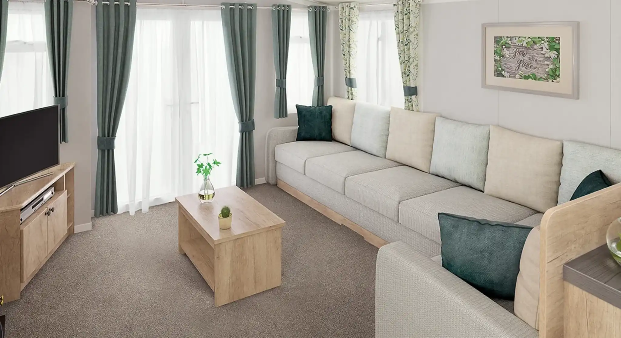 A modern living room featuring a spacious grey sectional sofa with light green and teal throw pillows. There is a wooden coffee table in the center and a television on a wooden stand. Natural light streams in through sheer curtains, illuminating the space adorned with leafy patterned drapes.