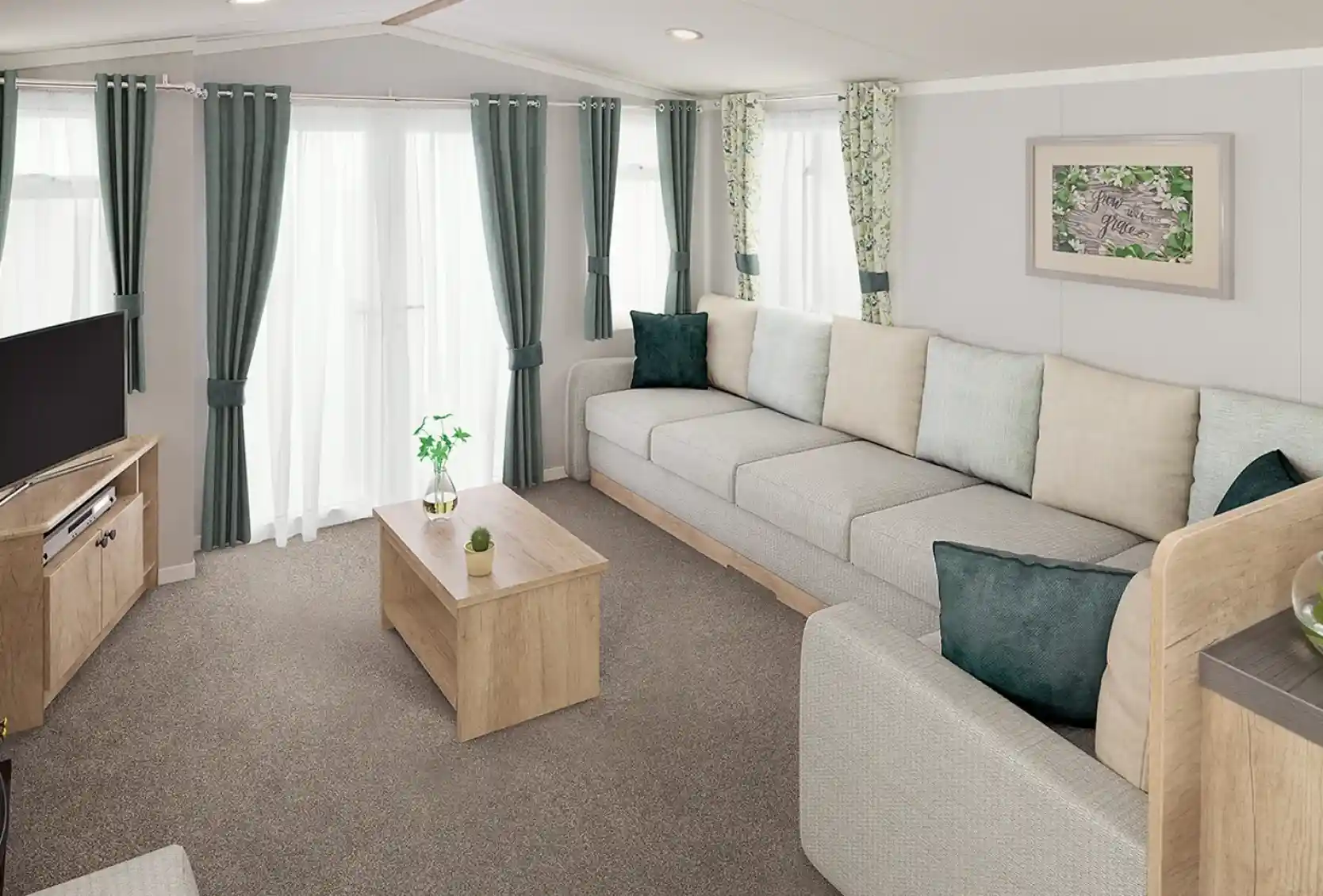 A modern living room featuring a spacious grey sectional sofa with light green and teal throw pillows. There is a wooden coffee table in the center and a television on a wooden stand. Natural light streams in through sheer curtains, illuminating the space adorned with leafy patterned drapes.