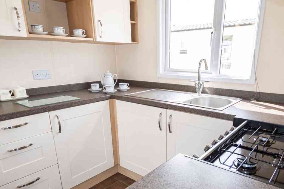 Bright kitchen with white cabinetry and dark countertops. A window over the sink lets in natural light. Teacups and a teapot sit neatly on the counter.