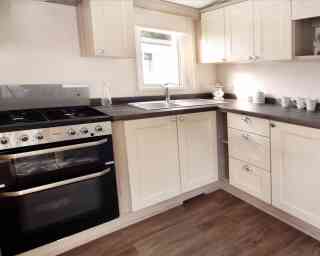 Bright, modern kitchen and living area in neutral tones with wood accents. Dining table set for two, floral curtains, and cozy seating enhance warmth.