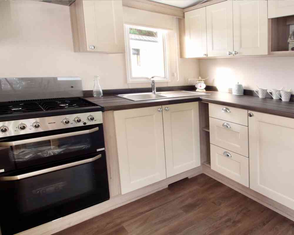 Bright, modern kitchen and living area in neutral tones with wood accents. Dining table set for two, floral curtains, and cozy seating enhance warmth.