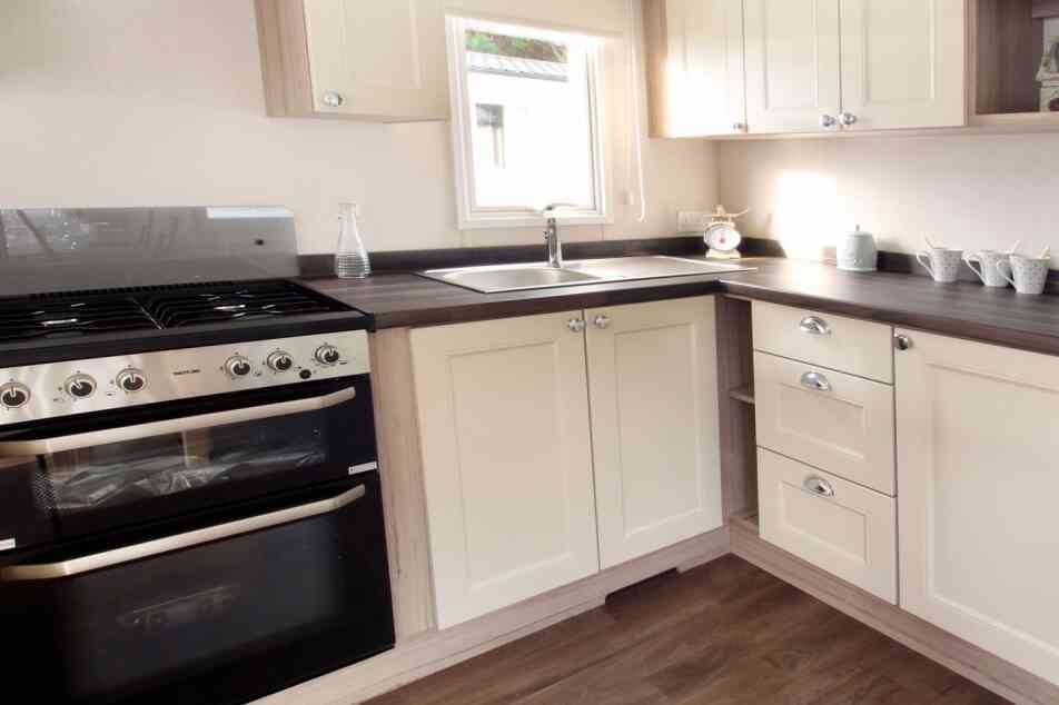 Bright, modern kitchen and living area in neutral tones with wood accents. Dining table set for two, floral curtains, and cozy seating enhance warmth.