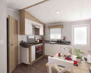 Modern kitchen interior with wooden and white cabinets, stainless steel oven, black countertops, and a cosy dining area decorated with plants and colourful fruit.
