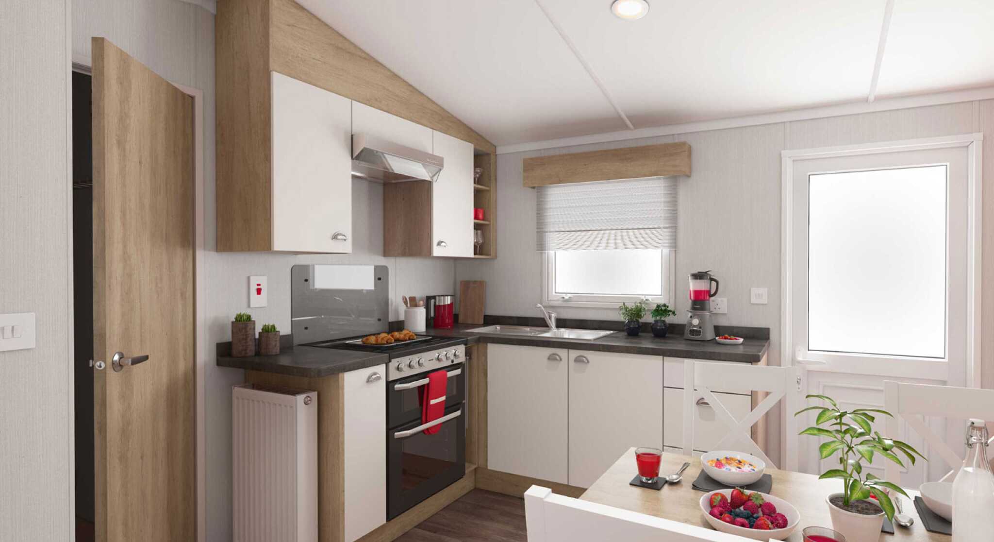 Modern kitchen interior with wooden and white cabinets, stainless steel oven, black countertops, and a cosy dining area decorated with plants and colourful fruit.