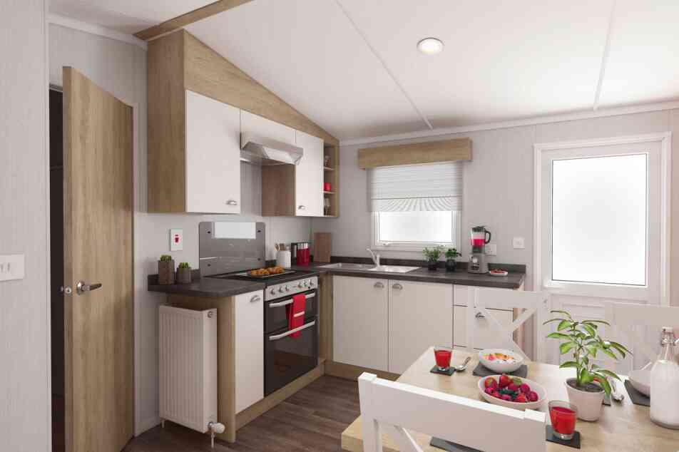 Modern kitchen interior with wooden and white cabinets, stainless steel oven, black countertops, and a cosy dining area decorated with plants and colourful fruit.