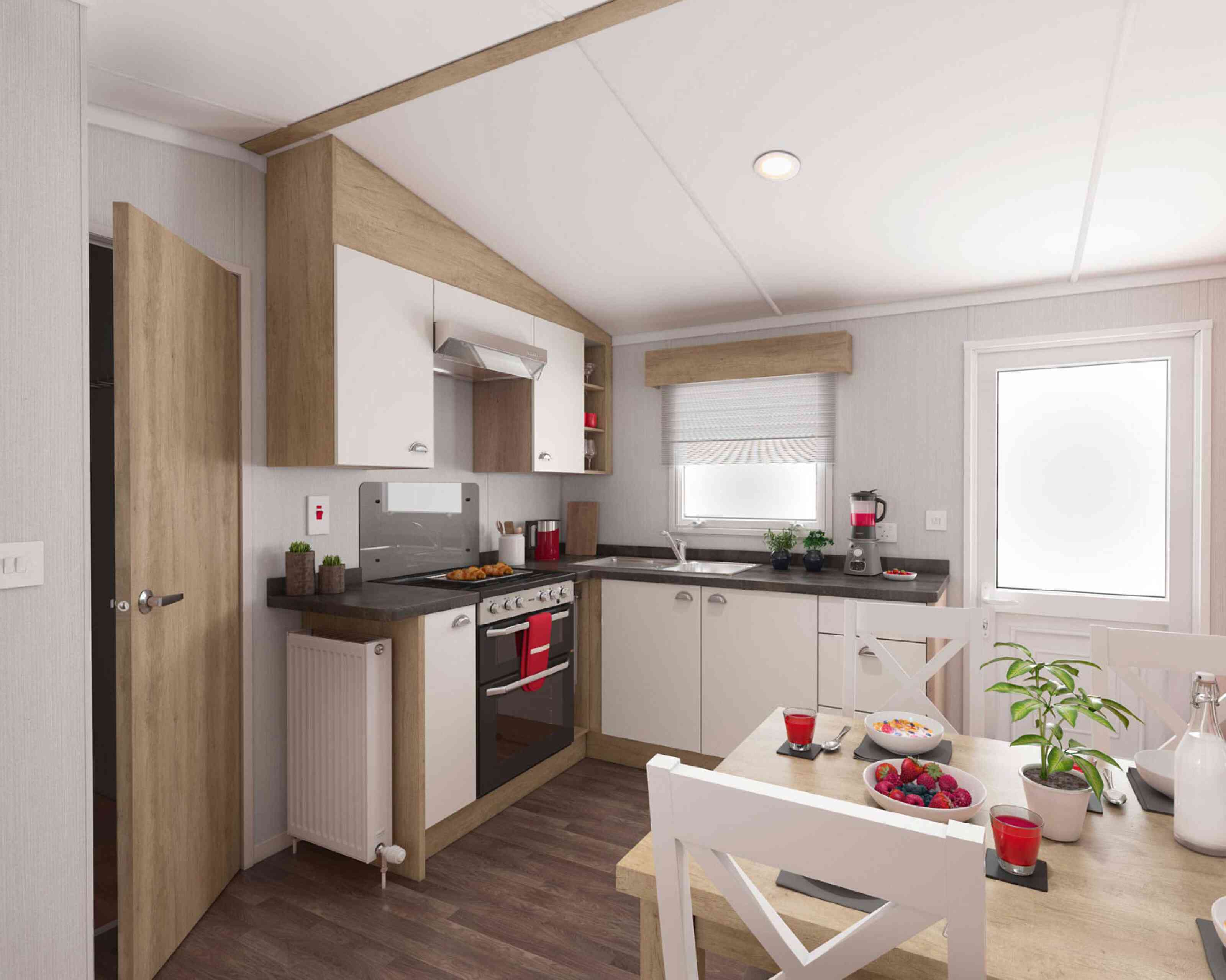 Modern kitchen interior with wooden and white cabinets, stainless steel oven, black countertops, and a cosy dining area decorated with plants and colourful fruit.