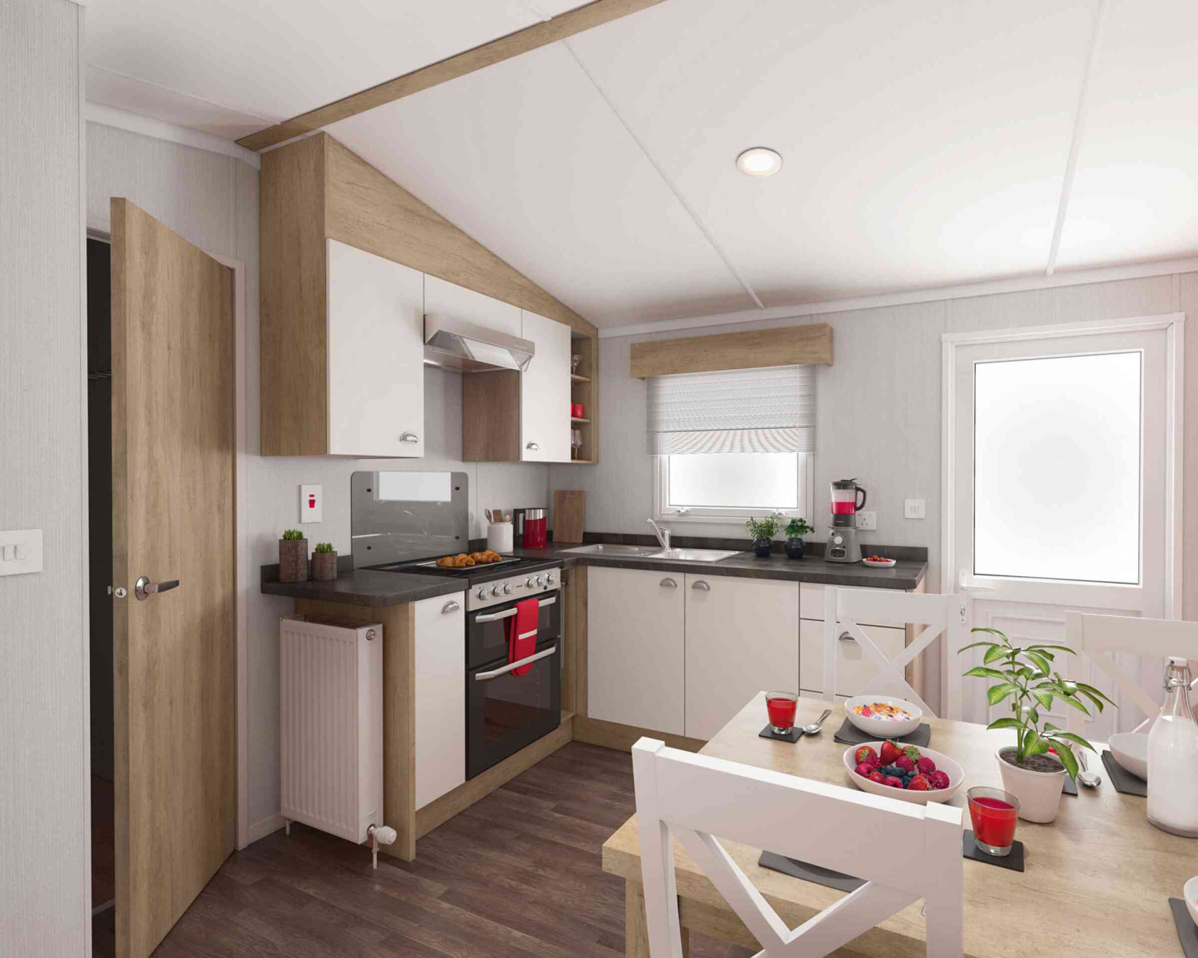 Modern kitchen interior with wooden and white cabinets, stainless steel oven, black countertops, and a cosy dining area decorated with plants and colourful fruit.