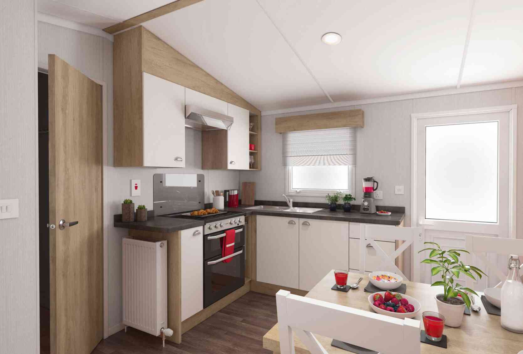 Modern kitchen interior with wooden and white cabinets, stainless steel oven, black countertops, and a cosy dining area decorated with plants and colourful fruit.