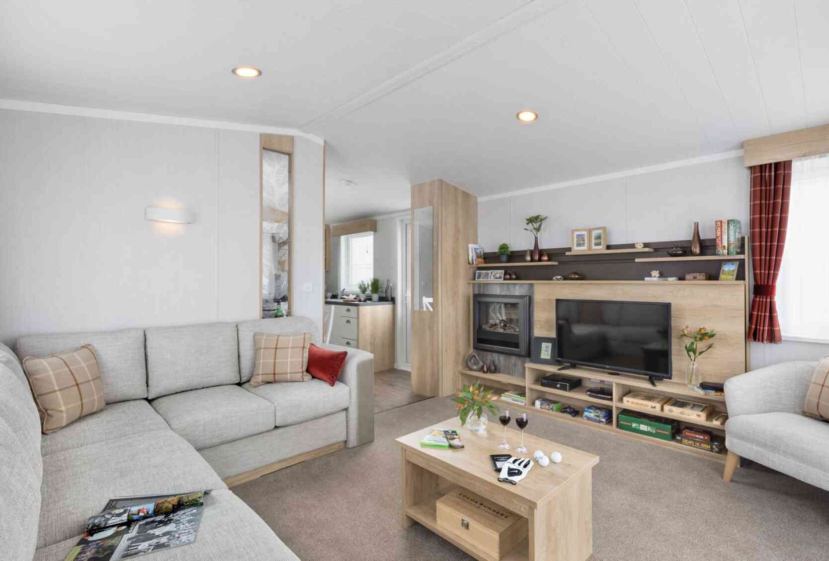 Inviting contemporary lounge featuring a grey corner sofa with patterned cushions, coffee table, TV, shelves, and soft, welcoming accents.