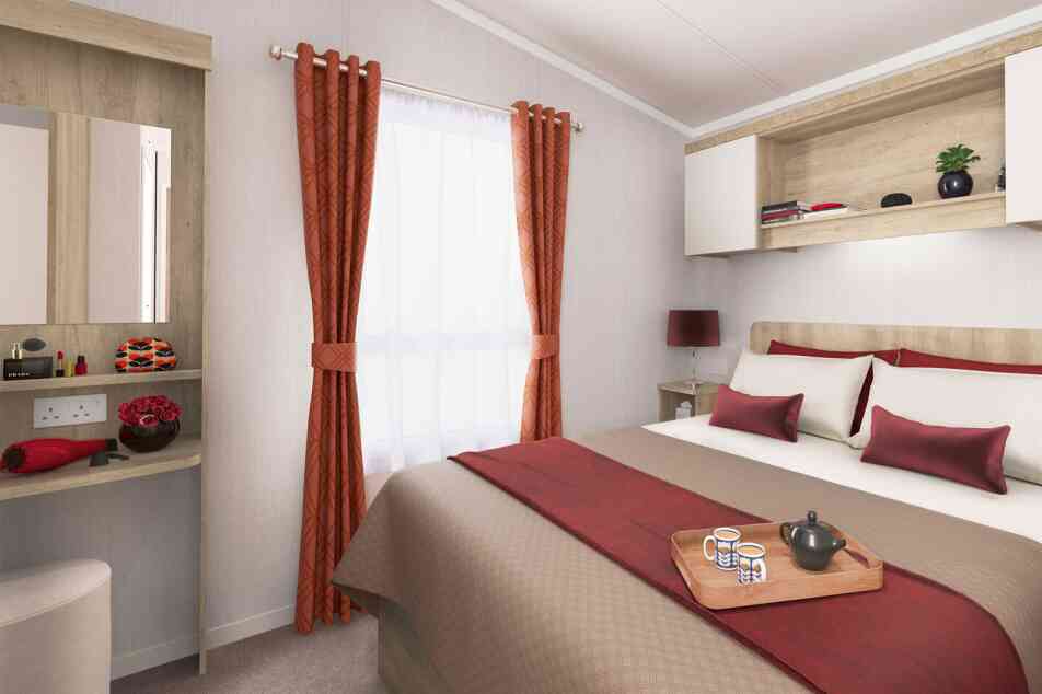 Inviting bedroom featuring a double bed with red and beige linens, a window with red curtains, bedside lighting, and wooden shelving.