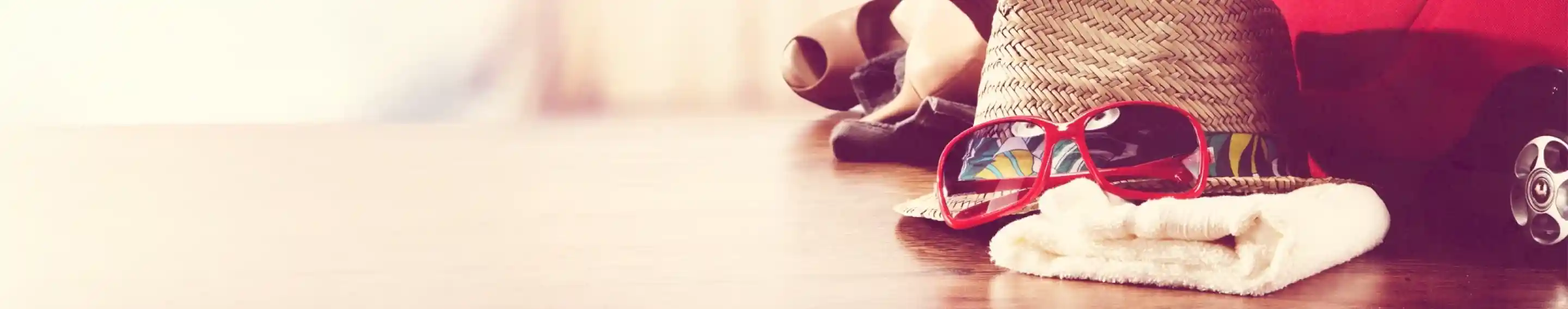 A sun hat with sunglasses resting on a towel, next to a red cooler and rolled-up beach towels, set against a soft, blurred background suggesting a sunny day.
